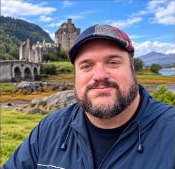 Joseph Estes smiling outdoors near a castle and loch